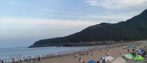 A beach with tents and people, a clear sky, and a hilly landscape in the background.