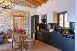 Uma cozinha moderna com armários escuros, uma parede de pedra e um espaço de refeições com cadeiras de madeira e uma mesa.