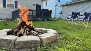 Un patio trasero con un pozo de fuego, césped y una casa de fachada azul.