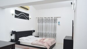 Une chambre à coucher comprenant un lit, une table de chevet, une lampe, un appareil de climatisation et un petit meuble.