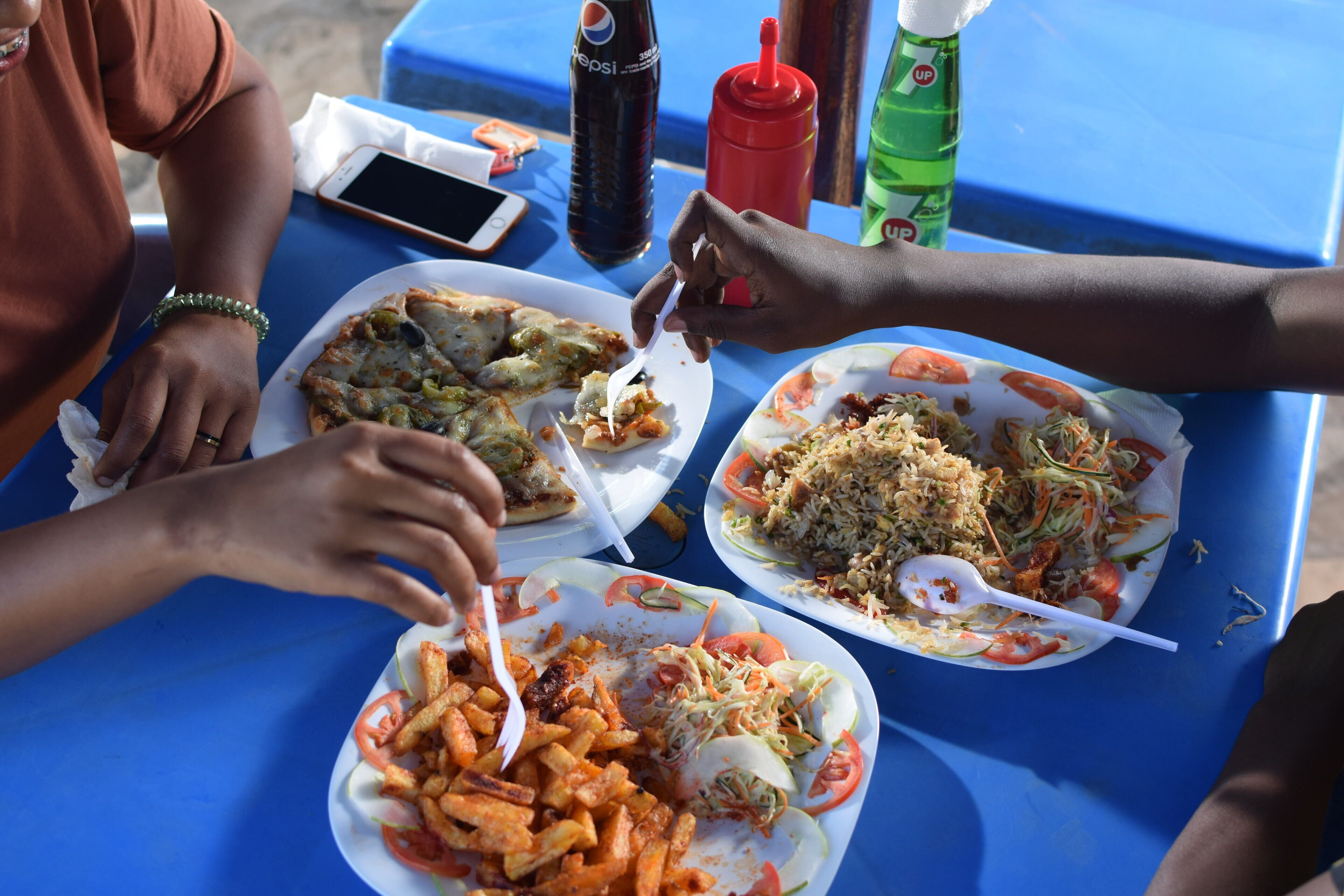 A table with various food items, including a plate of fries, a salad, and a rice dish, along with condiments and a smartphone.