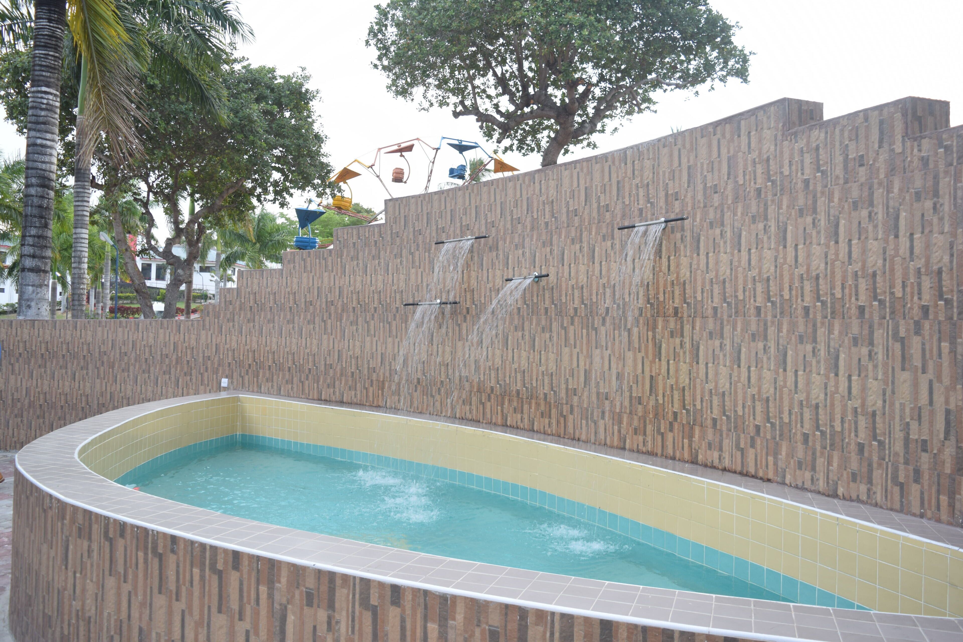 En swimmingpool med flisekant og en væg med lodrette trælameller.