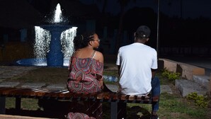 Deux personnes sont assises sur un banc devant une fontaine, la nuit.