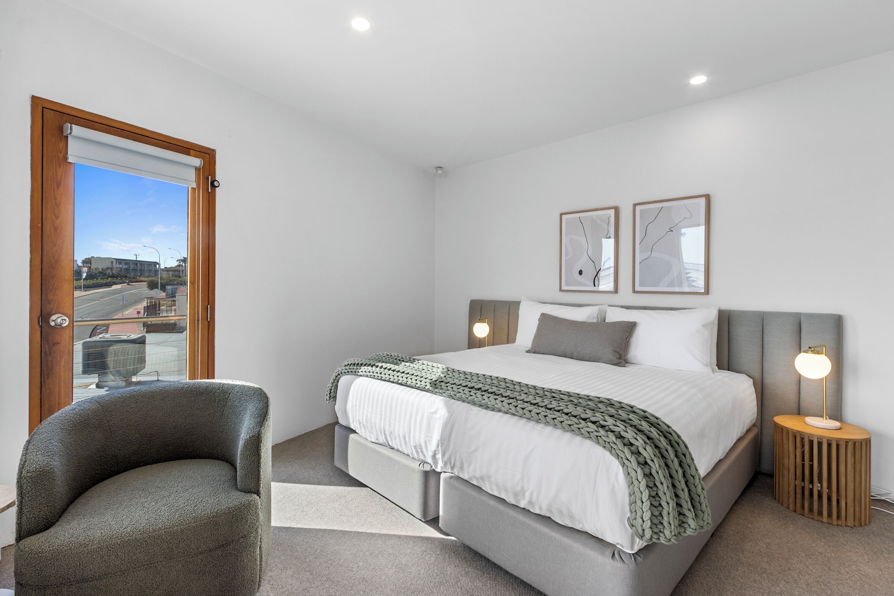 A bedroom with a bed, a chair, a bedside table with a lamp, and two framed pictures on the wall.
