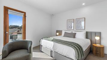 A bedroom with a bed, a chair, a bedside table with a lamp, and two framed pictures on the wall.