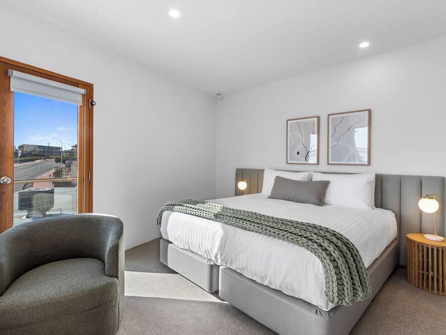 A bedroom with a bed, a chair, a bedside table with a lamp, and two framed pictures on the wall.
