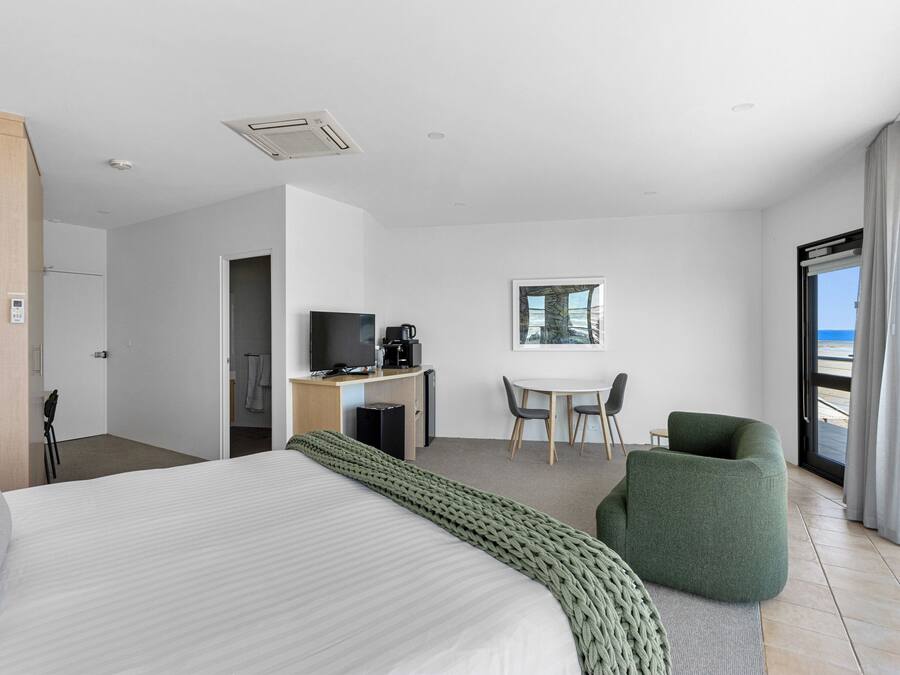 A hotel room with a large bed, a desk with a computer and coffee maker, a chair, and a view of the ocean.