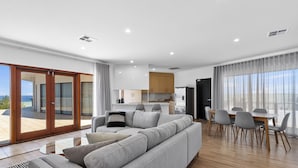Ein modernes Wohnzimmer mit einer großen grauen Couch, einem Esstisch mit Stühlen und einer Küche im Hintergrund.