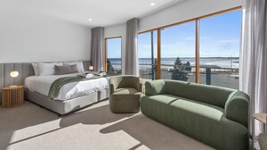 Ein modernes Schlafzimmer mit einem großen Bett, einer grünen Couch und Blick aufs Meer.