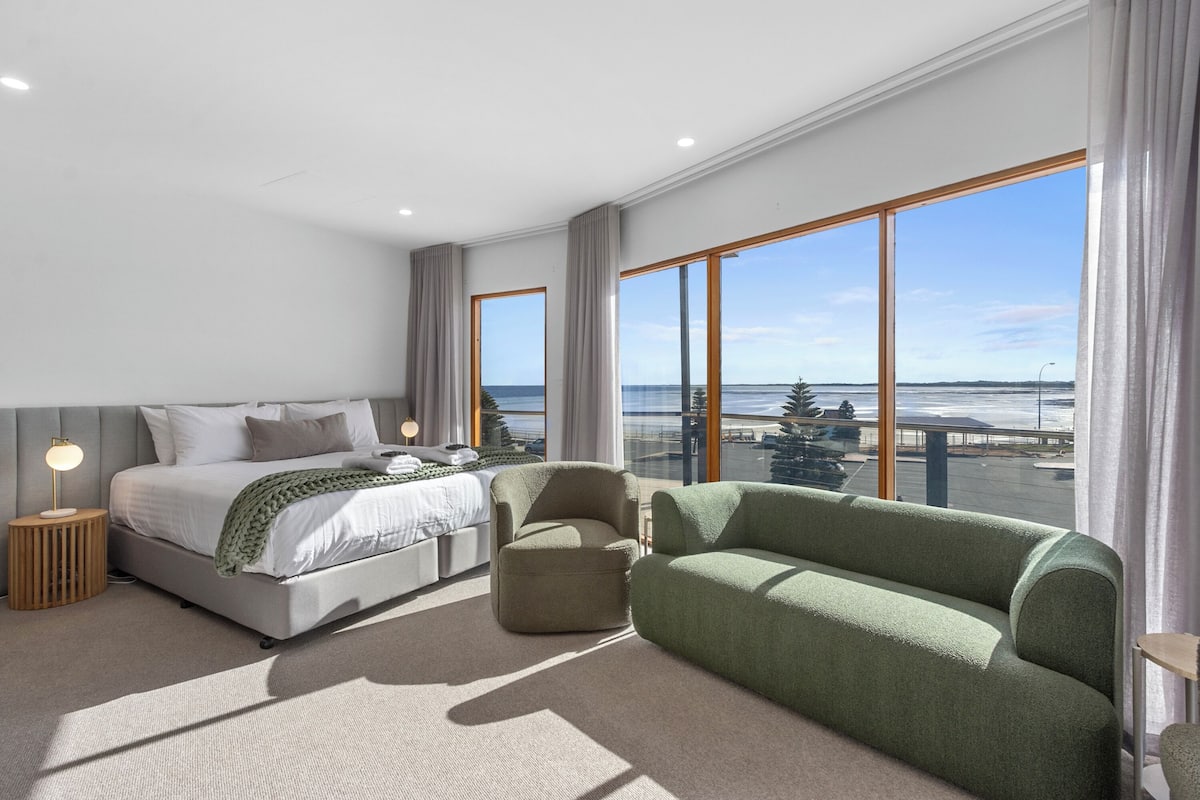 Un dormitorio moderno con una cama grande, un sofá verde y vistas al mar.