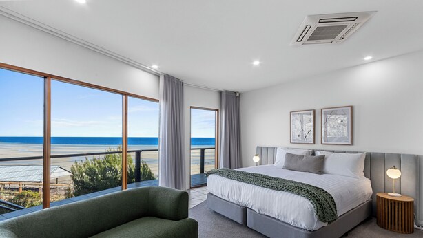 Ein modernes Schlafzimmer mit einem großen Bett, einem grünen Sessel und Blick auf den Strand.