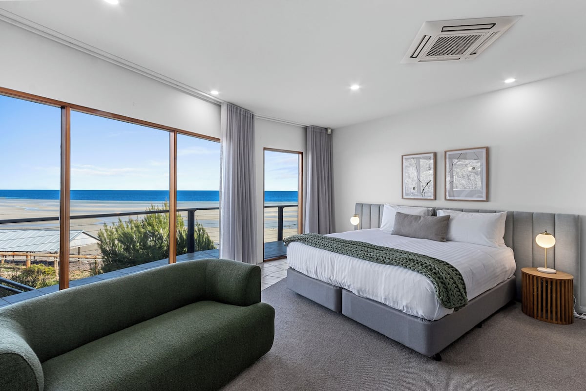 Un dormitorio moderno con una cama grande, un sillón verde y vista a la playa.