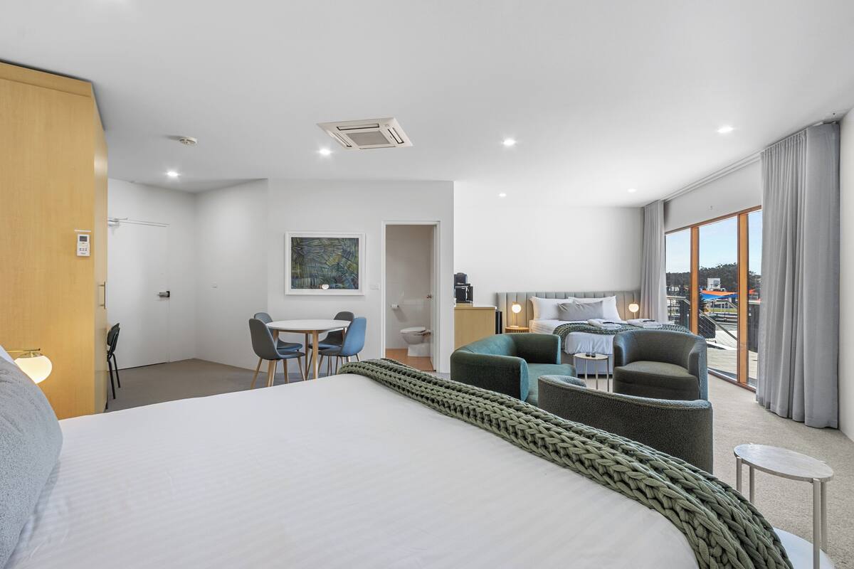 Una habitación de hotel moderna con una cama grande, un escritorio con silla, un sofá y un balcón con vistas.