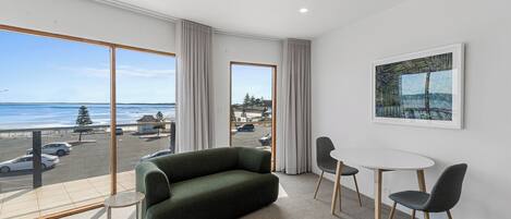 A modern hotel room with a large window offering a view of the beach and parking area.