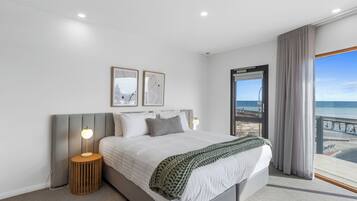 Un dormitorio moderno con una cama grande, una mesita de noche, una lámpara y vistas a la playa.
