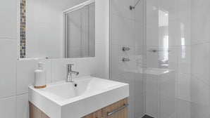 Ein Badezimmer mit einem weißen Waschbecken, einem Spiegel und einer Dusche.