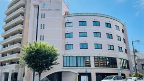 A multi-story building with a curved facade, balconies, and a tree in front. - BUSINESS HOTEL KUDAMATSU (Kudamatsu)