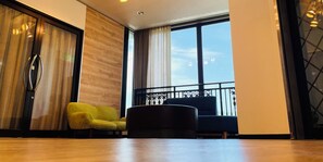 A modern living room with a wooden floor, a yellow armchair, a black sofa, and a large window with a view of tall buildings. - BUSINESS HOTEL KUDAMATSU (Kudamatsu)