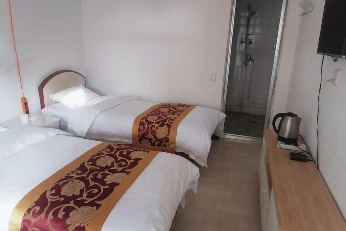 A hotel room with two beds, a shower, a TV, and a bedside table with a kettle.