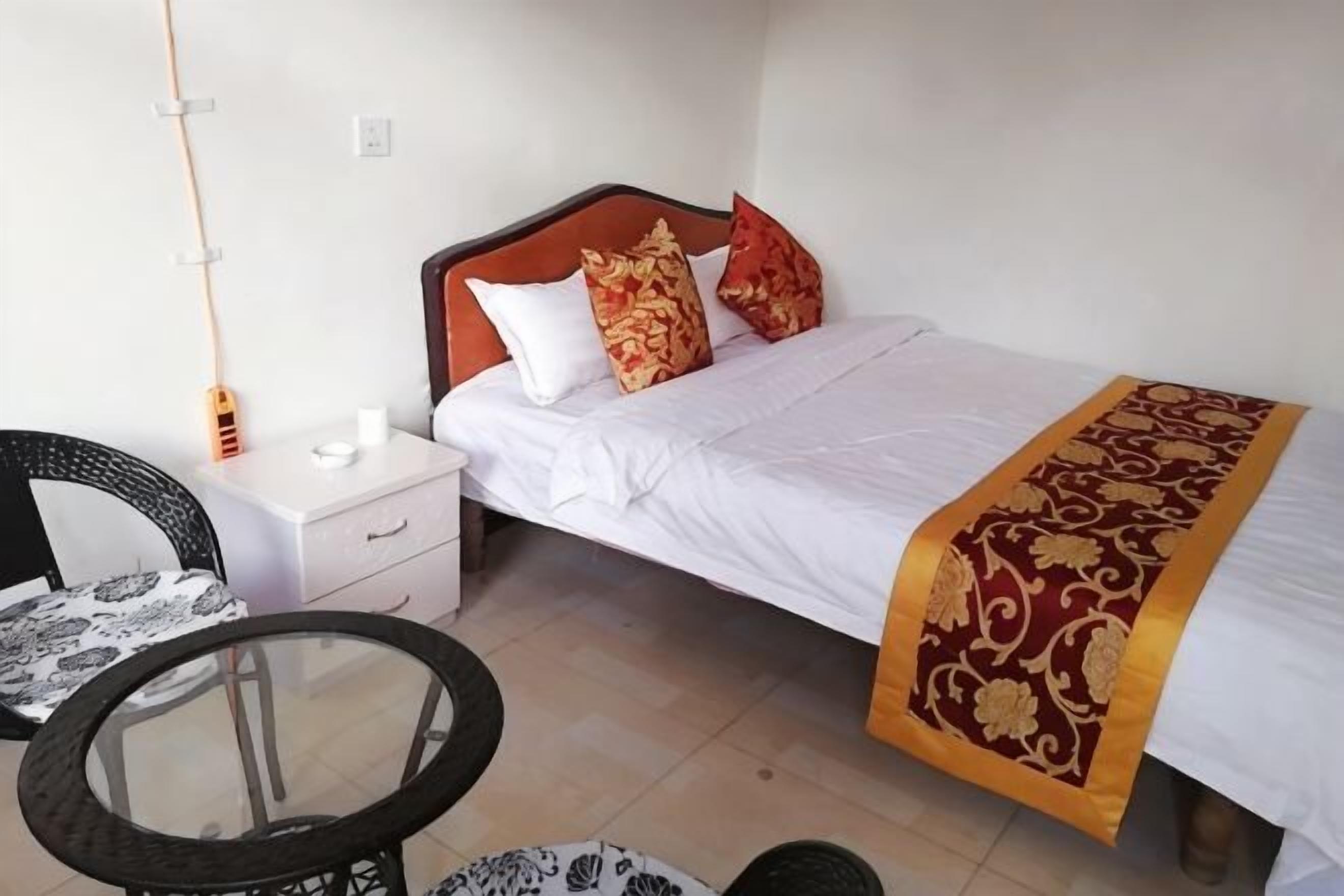 A single bed with a white and red bedspread, a wooden headboard, and a bedside table with a lamp.