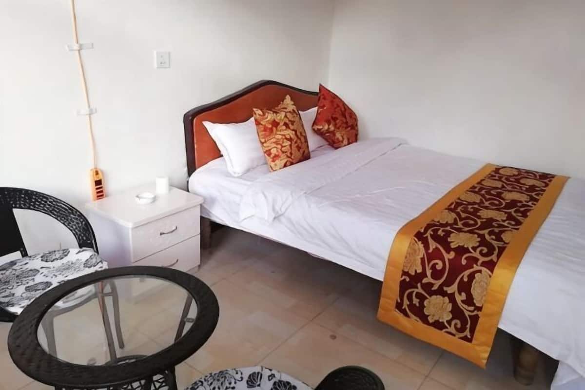 A single bed with a white and red bedspread, a wooden headboard, and a bedside table with a lamp.