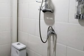 Ein Badezimmer mit weißen Fliesen, einer Dusche inklusive Handbrause und einem kleinen Mülleimer.