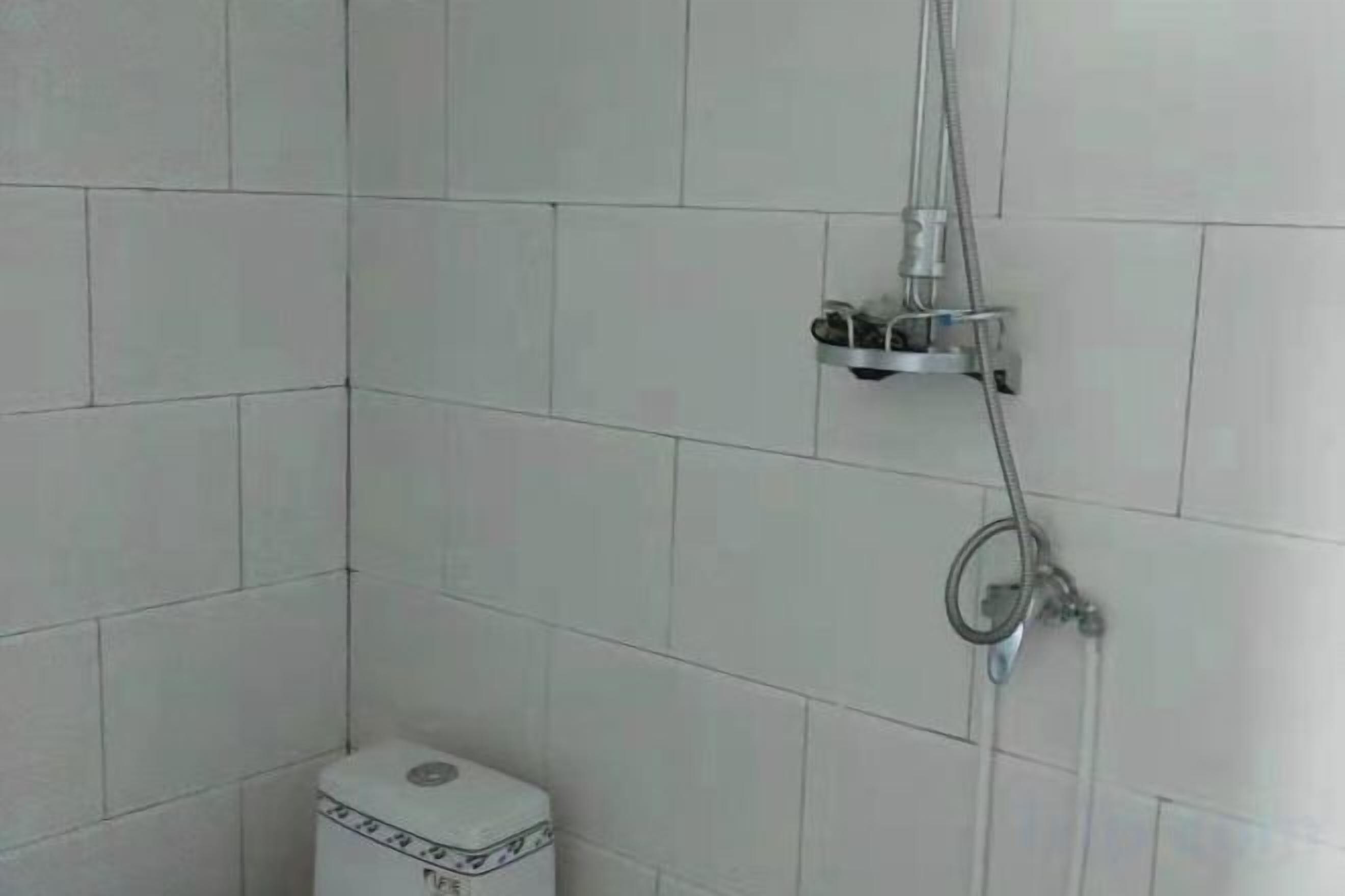 A bathroom with white tiled walls, a toilet, and a shower with a handheld showerhead and a wall-mounted faucet.
