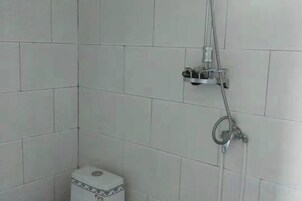 Un baño con paredes de azulejos blancos, un inodoro y una ducha con cabezal de ducha manual y grifo empotrado.