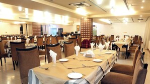Une grande salle à manger avec de nombreuses tables dressées pour le service, chacune étant recouverte d’une nappe et agrémentée de couverts disposés avec soin.