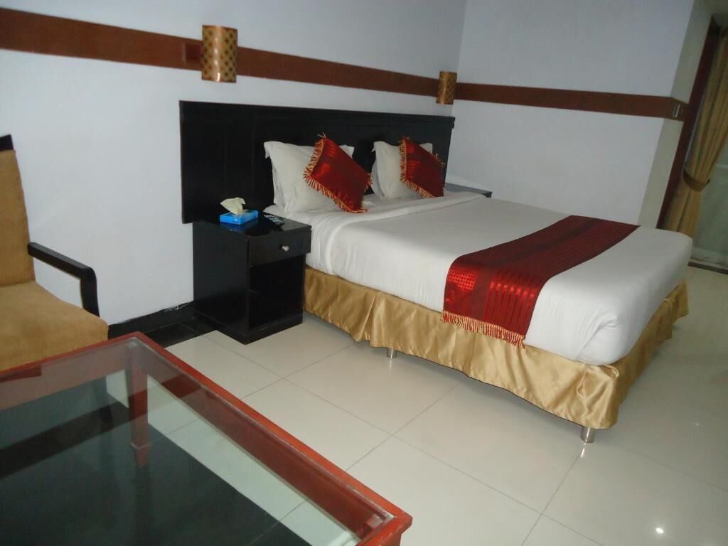 A hotel room with a bed, a nightstand, a glass table, and a chair.