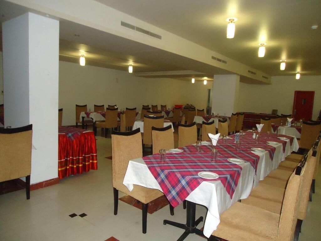 Un comedor con varias mesas dispuestas para el servicio, sillas alrededor de cada una, y una cortina roja en la entrada.