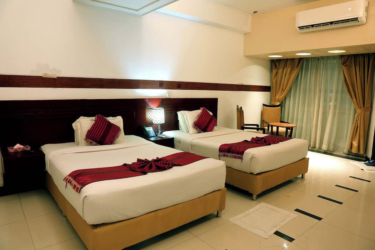 A hotel room with two beds, a desk, a chair, an air conditioner, and a window with curtains.