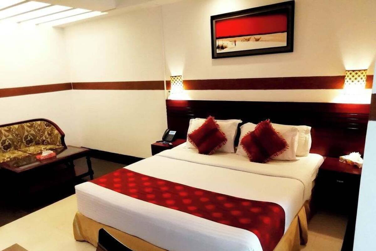 A hotel room with a large bed, two bedside tables, a nightstand, a sofa, and a framed picture on the wall.