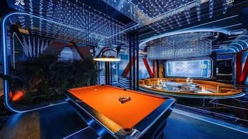 A modern pool table with a bar area and a large screen in a futuristic room.