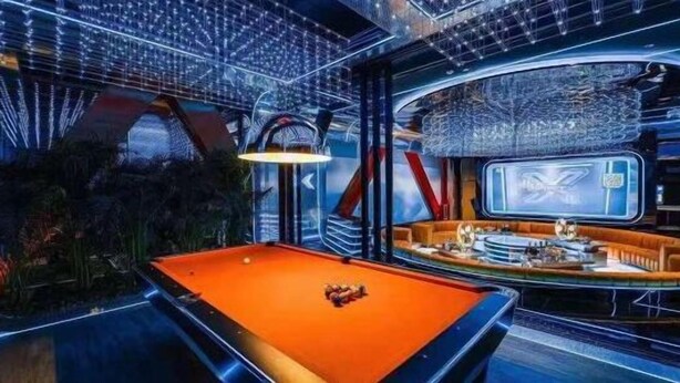 A pool table with a billiard cue and balls, a bar area with stools, and a large screen displaying a logo. - Yiting Business Hotel (Quanzhou)