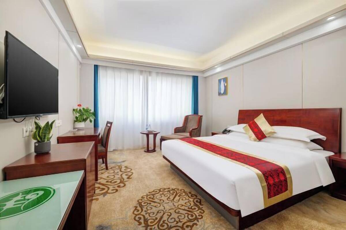 Une chambre d’hôtel avec un grand lit, un bureau, une chaise, une télévision et une fenêtre avec des rideaux.