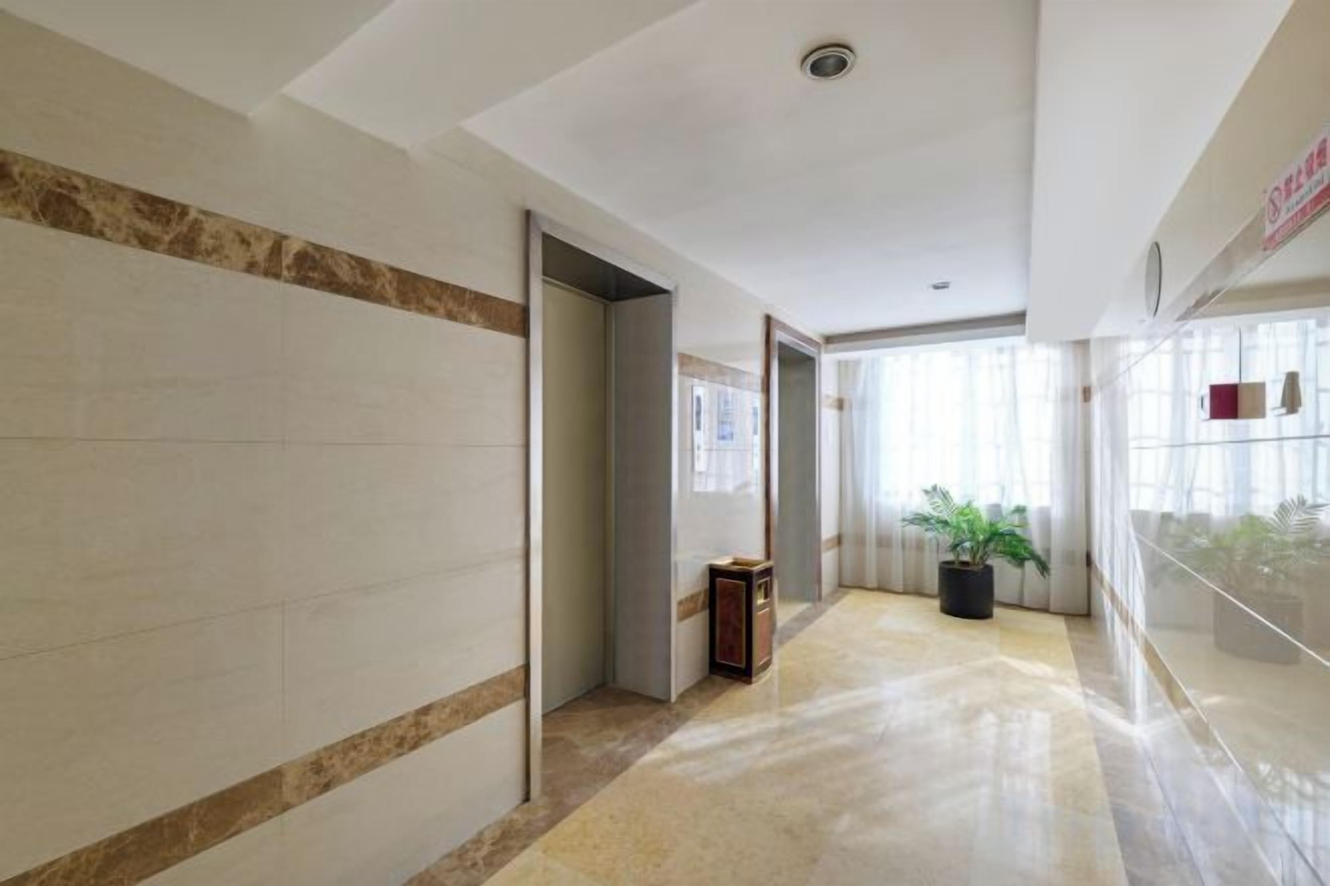 Un pasillo con piso de mármol, una puerta y una planta en maceta.