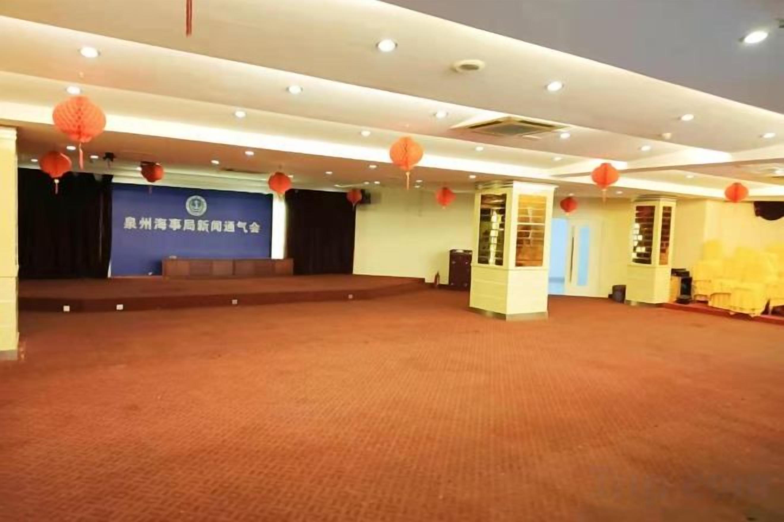 Un amplio salón con un escenario, faroles rojos y un estandarte azul.