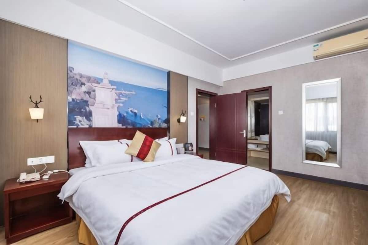 Une chambre d’hôtel avec un grand lit, une table de chevet, une lampe fixée au mur, un miroir et une vue sur la mer.