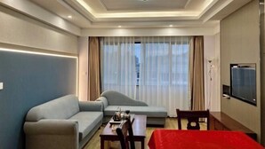 A hotel room with a sofa, a dining table with chairs, a TV mounted on the wall, and a large window with curtains. - Yiting Business Hotel (Quanzhou)