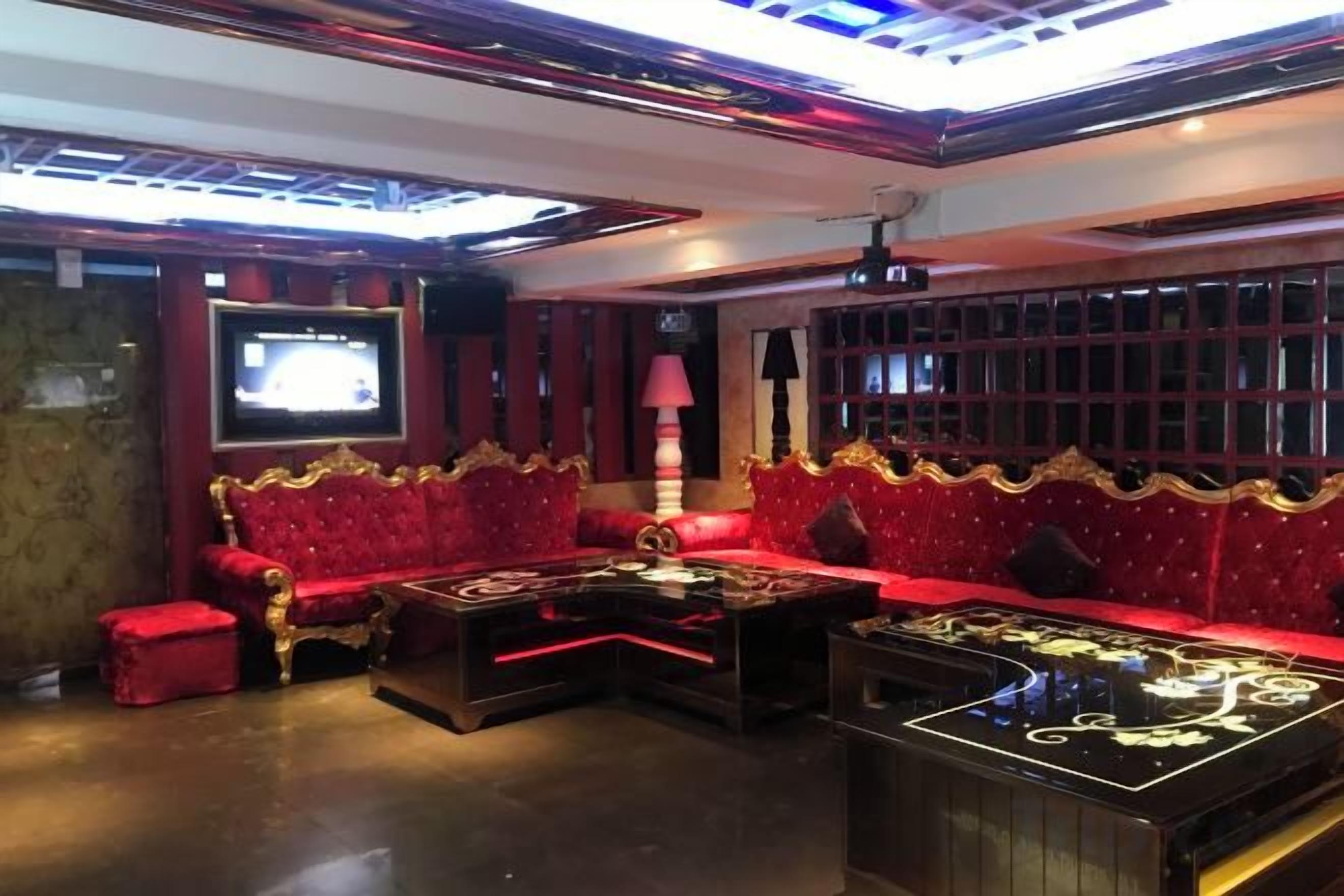 Una habitación con un sofá tapizado rojo, una mesa de centro negra con detalles dorados y un televisor montado en la pared.