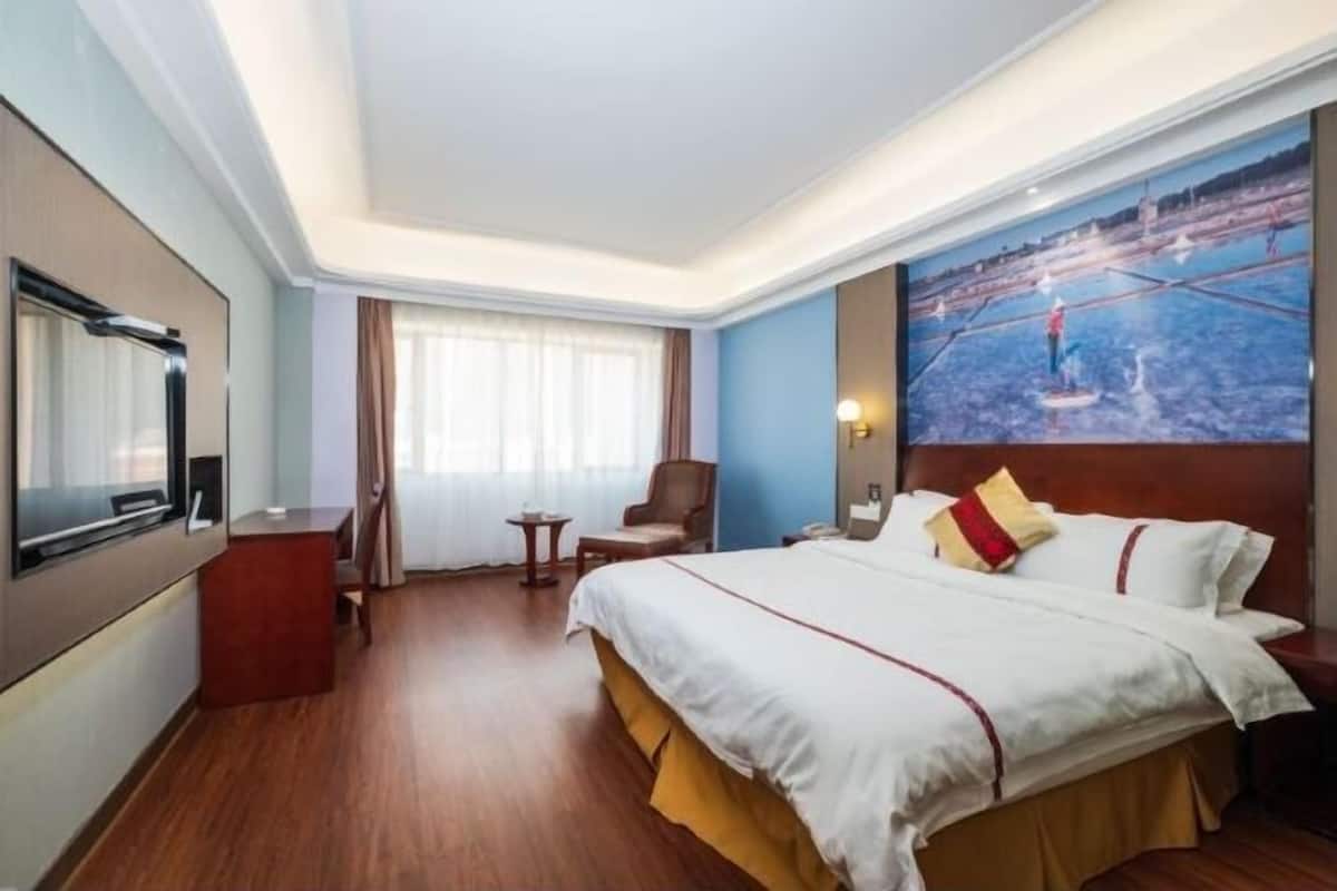 Une chambre d’hôtel avec un grand lit, un téléviseur à écran plat, une petite table, une chaise et un tableau au mur.