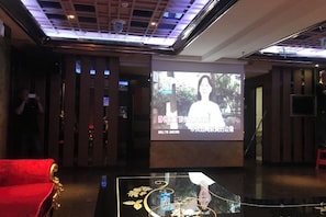 A lobby with a red sofa, a projection screen displaying a person, and a glass table with a decorative item. - Yiting Business Hotel (Quanzhou)