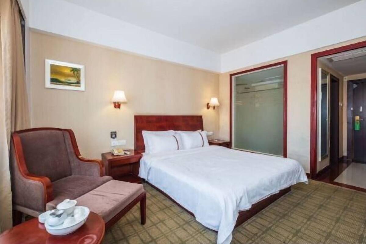 Une chambre d’hôtel avec un lit, une chaise, une table de chevet et une lampe fixée au mur.