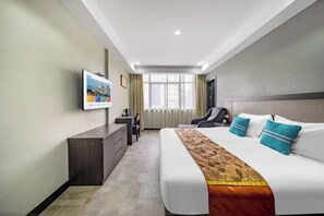 Een moderne hotelkamer met een groot bed, een bureau, een stoel en een aan de muur bevestigde televisie.