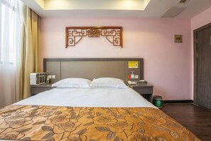 Een hotelkamer met een bed, nachtkastje, decoratie aan de muur en een afvalbak.
