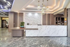Un área de recepción con mostrador de mármol, iluminación colgante y una planta en maceta.