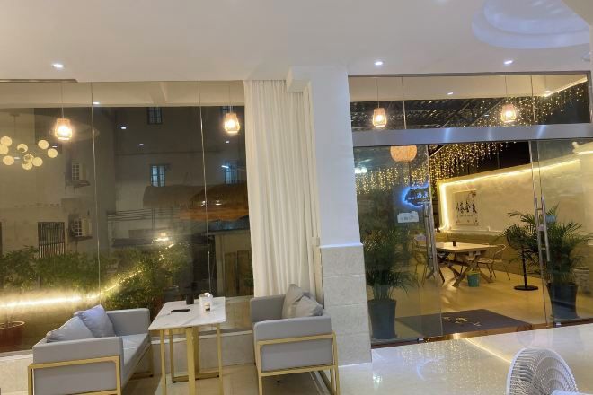A modern hotel lobby with a seating area, a reception desk, and a view of the interior through large glass doors.
