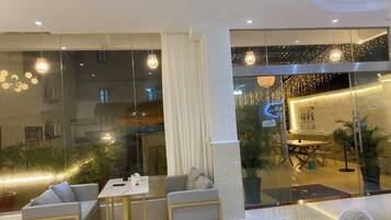 A modern hotel lobby with a seating area, a reception desk, and a view of the interior through large glass doors.