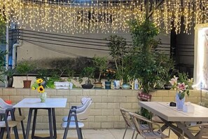 An outdoor patio with a table and chairs, surrounded by potted plants and a string of lights. - Alley See You Inn (Danxia Mountain Scenic Area) (Renhua)